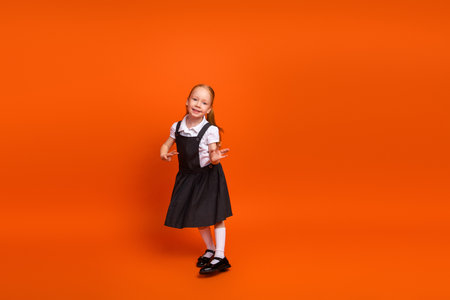 Schoolgirl in uniform against orange background joyfully posing and expressing happiness, representing back-to-school themesの写真素材