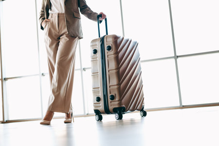Confident Businesswoman Alongside Stylish Suitcase, Ready for Travel in a Bright Corporate Settingの写真素材