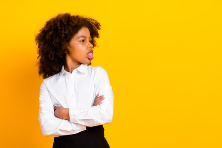 Confident young schoolgirl in formal attire with arms crossed against a vibrant yellow background showing an expressive gestureの写真素材