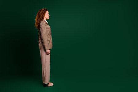 Confident young professional woman in a formal outfit standing against an emerald green background in studioの写真素材