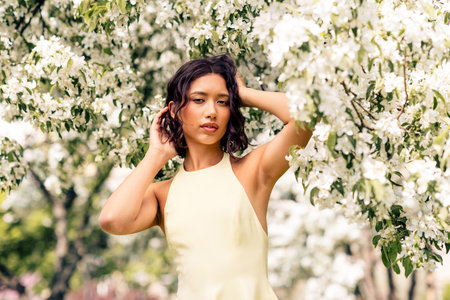 Young woman enjoys nature in a spring garden surrounded by blossoms on a bright sunny day, embracing...