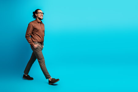 Young professional man walking confidently in stylish attire against a vibrant turquoise background for fashion and lifestyle themesの写真素材