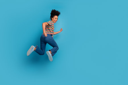 Young woman with vibrant hairstyle jumping against a turquoise background in casual striped t-shirt and jeansの写真素材
