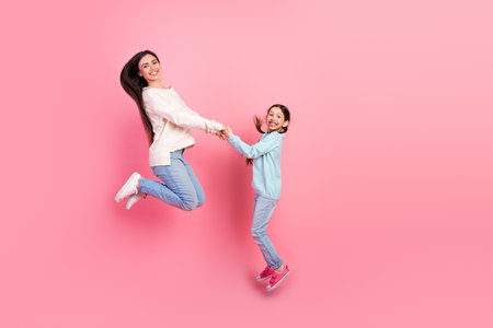Cheerful Mother and Daughter Jumping Together in Joy Against a Pink Backgroundの写真素材