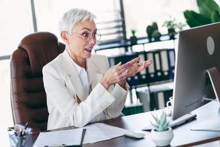 Professional senior businesswoman engaged in virtual communication from her organized and stylish modern office workspaceの写真素材