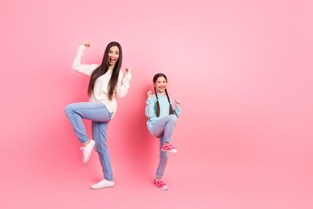 Cheerful young woman and little girl bonding in casual wear posing joyfully against a pink backgroundの写真素材