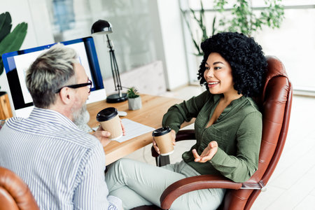 Two professionals engaging in a productive discussion while holding coffee cups in a modern and bright office setting.の写真素材