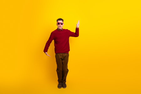 Cheerful Young Stylish Man Gesturing on Yellow Background in Casual Red Sweaterの写真素材