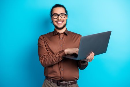 Young professional man presenting with a laptop wearing formalwear on teal background showcasing...