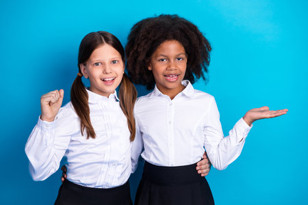 Cheerful young schoolgirls in uniform posing against a blue background showcasing friendly gestures and vibrant personalitiesの写真素材