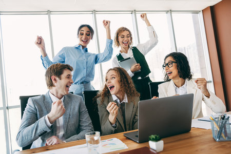 Excited team celebrating success during a collaboration meeting in a modern workplace setting with diverse professionalsの写真素材