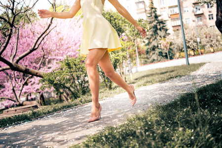 Lovely woman in a yellow dress walking joyfully through a vibrant park during springtime, surrounded by blooming treesの写真素材