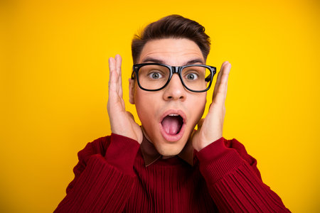 Surprised Young Man in Glasses Against Vibrant Yellow Background, Expressive Gestureの写真素材