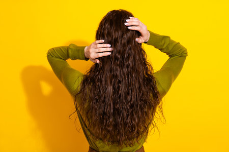 Young woman with long brunette hair wearing green shirt posing against a bright yellow background...