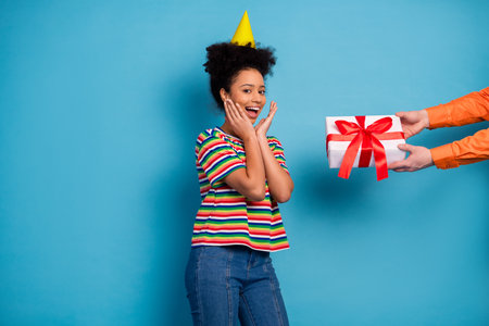 Smiling young woman in a striped shirt celebrates her birthday with a surprise present against a turquoise backgroundの写真素材