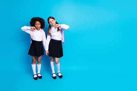 Two young schoolgirls in uniform express contrasting emotions on a bright blue background, symbolizing diversity and friendshipsの写真素材
