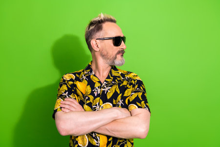 Charismatic gentleman in a vibrant tropical shirt posing against a green backdrop during summertime celebrationの写真素材