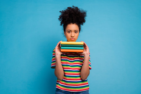 Young woman in colorful striped shirt holding books against a turquoise background, showcasing vibrant and casual styleの写真素材