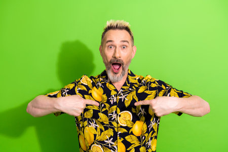 Charismatic man in a vibrant lemon-printed shirt expressing joy against a bright green background, highlighting summer vibesの写真素材