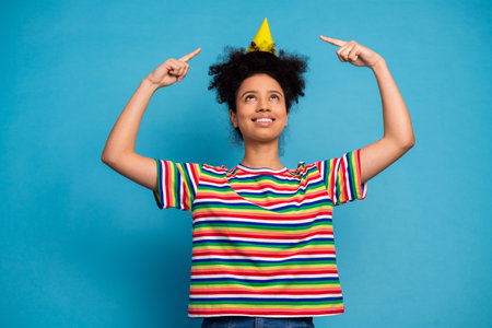 Happy young woman wearing a colorful striped t-shirt celebrating with a cone hat against vibrant...