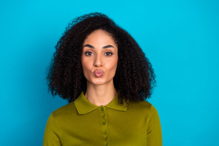 Charming Woman Posing with a Kiss Gesture Wearing Green Outfit Against a Blue Background in a Fun Styleの写真素材