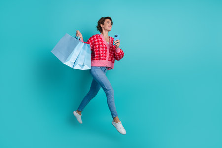 Full length photo of positive shiny lady wear pink cardigan holding shoppers typing device emtpy space isolated teal color backgroundの写真素材