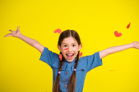 Adorable girl in blue outfit smiling joyfully with arms outstretched against vibrant yellow backgroundの写真素材
