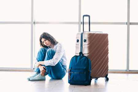 Young woman sitting on the floor with luggage at an airport terminal, waiting for departure and air travelの写真素材