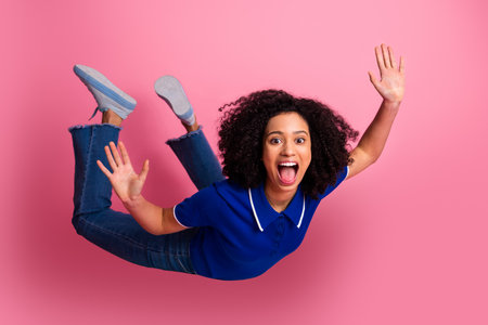 Excited young woman with curly hair in casual fashion jumps for joy against a vibrant pink...