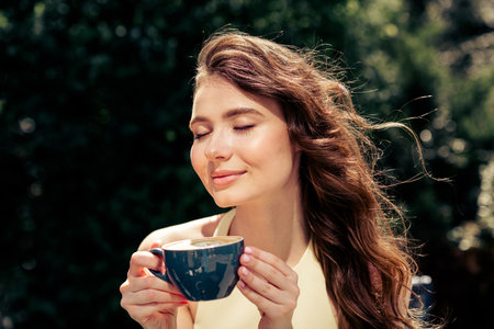Young woman enjoys relaxing outdoors on a sunny day holding a coffee cup and embracing peaceful leisure momentsの写真素材