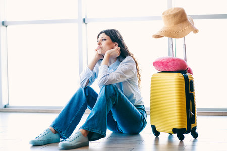 Passenger woman sitting at an airport terminal during her journey, with luggage and travel accessories, waiting calmlyの写真素材