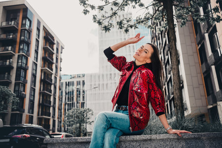 Stylish woman in red jacket posing in modern urban environment on a sunny day, exuding confidence...