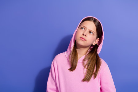 Portrait of a young girl wearing a pink hoodie looking thoughtful against purple backgroundの写真素材