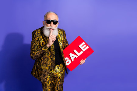 Confident gentleman in vibrant patterned suit holding a sale sign and making a thoughtful hand gesture against a vivid purple backgroundの写真素材