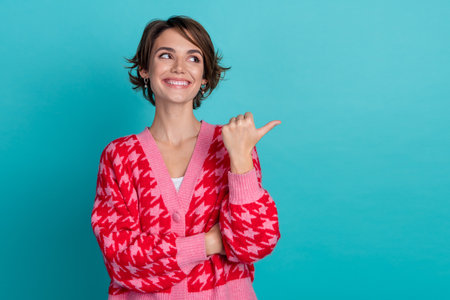 Photo of dreamy positive lady wear pink cardigan pointing thumb emtpy space isolated teal color backgroundの写真素材
