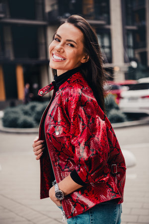 Young woman wearing stylish red jacket outdoors, smiling confidently with trendy urban background on...