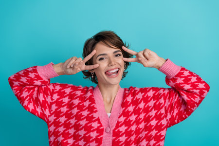 Photo portrait of pretty young girl show v-sign posing face wear trendy red outfit isolated on aquamarine color backgroundの写真素材