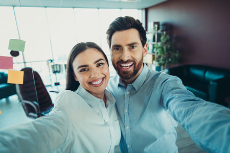 Smiling business professionals taking a selfie at a modern office workspace showcasing collaboration and teamworkの写真素材