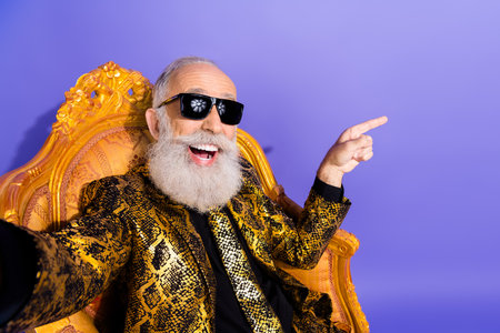 Elderly man in stylish golden suit and sunglasses posing confidently on luxurious chair with a...