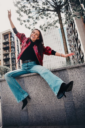 Young woman enjoying outdoor fun in stylish red jacket amidst urban cityscape, vertical photoの写真素材