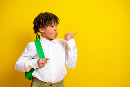 Young student posing with backpack on vibrant yellow background showcasing optimism and style during academic school yearの写真素材