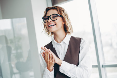 Confident Businesswoman Clapping Hands in Modern Office Setting on Bright Dayの写真素材