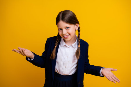 Confident schoolgirl in uniform smiling and gesturing against yellow background embracing learning and curiosityの写真素材