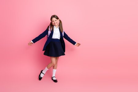 Happy schoolgirl in uniform posing on pink background, ready for school with a cheerful expression and stylish lookの写真素材