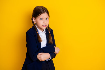 Young schoolgirl in uniform with concerned expression standing against yellow backgroundの写真素材