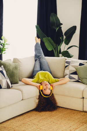 Positive woman wearing headphones relaxing on a cozy couch in a stylish living room with modern...