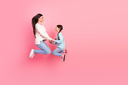 Mother and daughter joyfully jumping together in a pink studio setting, expressing love, bonding, and cheerful motherhood moments.の写真素材