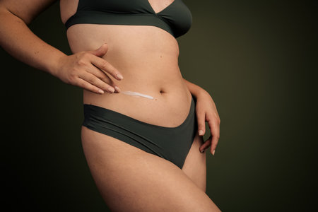 Close up of a woman applying skincare cream to her abdomen, embracing natural beauty with a focus on self care and body careの写真素材