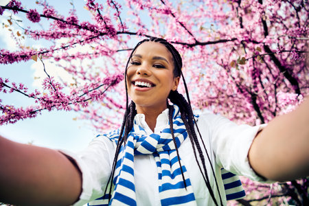 Cute woman with braided hair smiling in a blooming park enjoying a sunny spring day outdoors