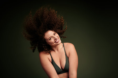 Confident young woman with curly brown hair posing in khaki sportswear against a green backgroundの写真素材